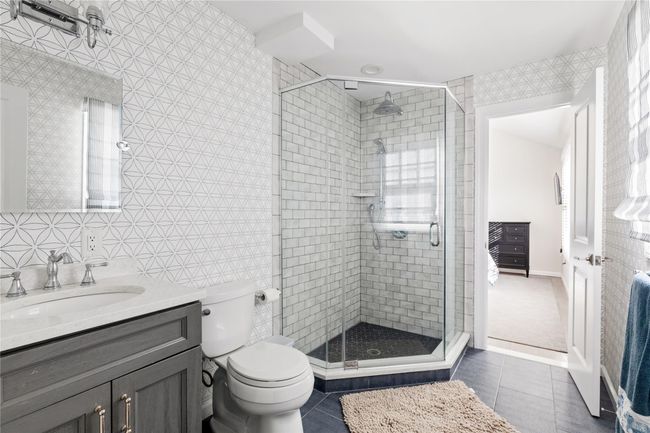 Bathroom with tile patterned floors, toilet, tile walls, a stall shower, and vanity | Image 45