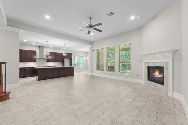 Love how the kitchen island flows into the living area—perfect for chatting while you cook. Dark wood cabinets contrast the light tile, and three big windows flood the space with natural light and backyard views. Cozy fireplace rounds it out for family movie nights or weekend gatherings. | Image 8