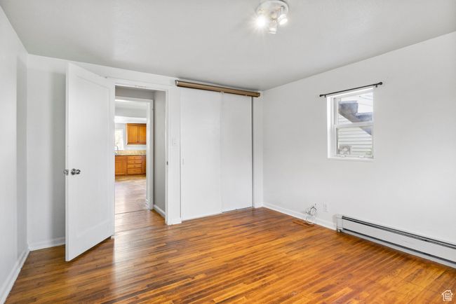 Unfurnished bedroom featuring wood finished floors, a baseboard heating unit, baseboards, and multiple windows | Image 44