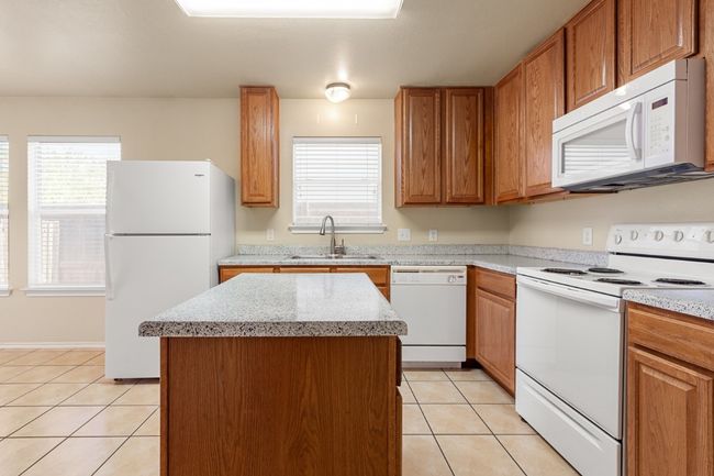 Kitchen featuring white appliances, light tile patterned floors, a center island, and brown cabinets | Image 10