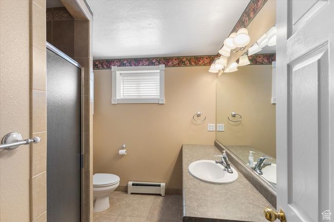 Full bathroom featuring vanity, a stall shower, tile patterned floors, toilet, and a baseboard radiator | Image 21