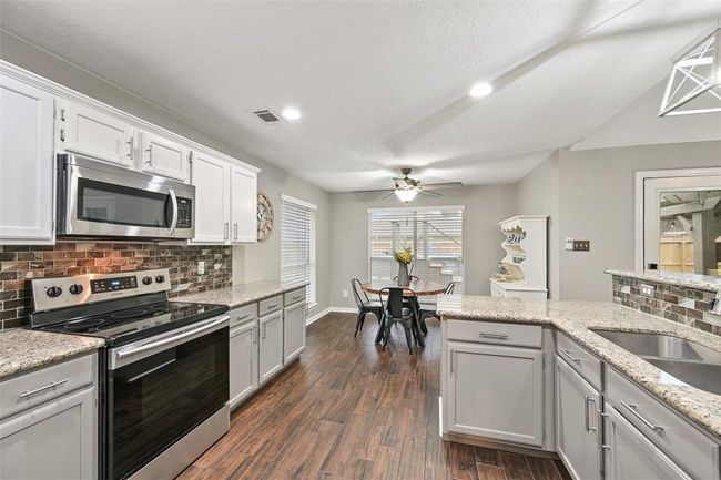 The open kitchen flows seamlessly into a sunny breakfast nook with backyard views, creating the perfect space for casual dining. Notice the all stainless appliances that include a 5-burner gas cooktop, a single oven, a vent hood. microwave, and a dishwasher. | Image 6