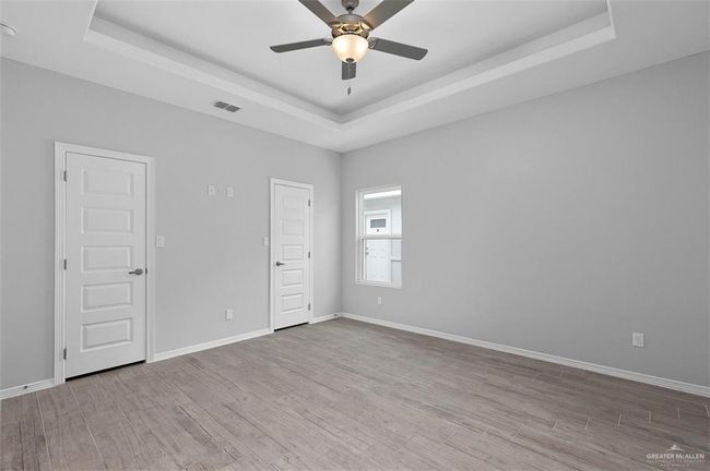 Empty room with a raised ceiling, wood finished floors, ceiling fan, and baseboards | Image 4