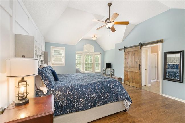 Bedroom with wood finished floors, vaulted ceiling, a barn door, ceiling fan, and baseboards | Image 30