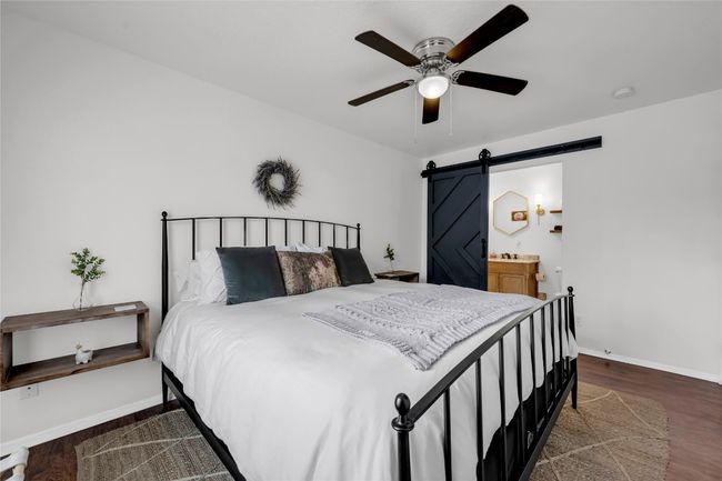 Bedroom with baseboards, a barn door, a ceiling fan, ensuite bathroom, and wood finished floors | Image 16