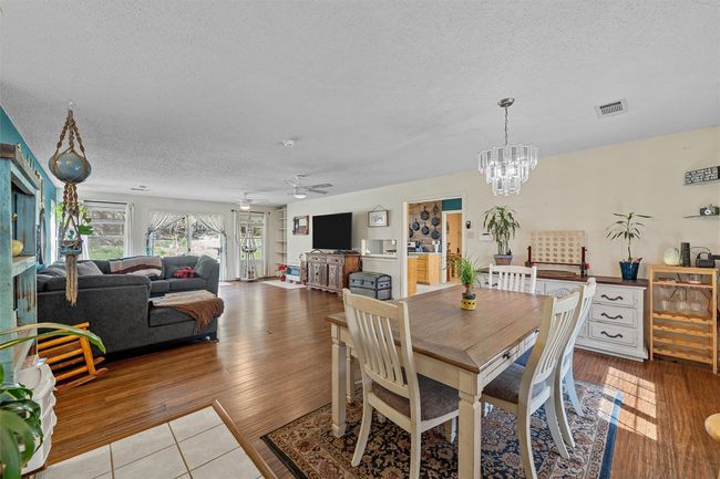 Dining space featuring a textured ceiling, wood finished floors, visible vents, and ceiling fan with notable chandelier | Image 6