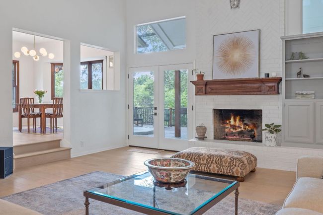 Living area with wood finished floors, a brick fireplace, a towering ceiling, a chandelier, and french doors | Image 6