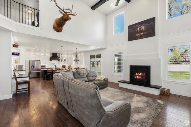 Living area featuring dark wood-type flooring, a healthy amount of sunlight, a towering ceiling, and a warm lit fireplace | Image 8