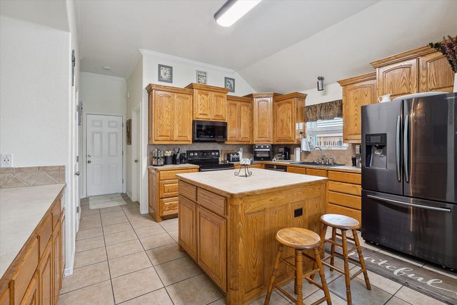 Kitchen featuring, black range with electric stovetop, light tile patterned floors, and a center island | Image 10