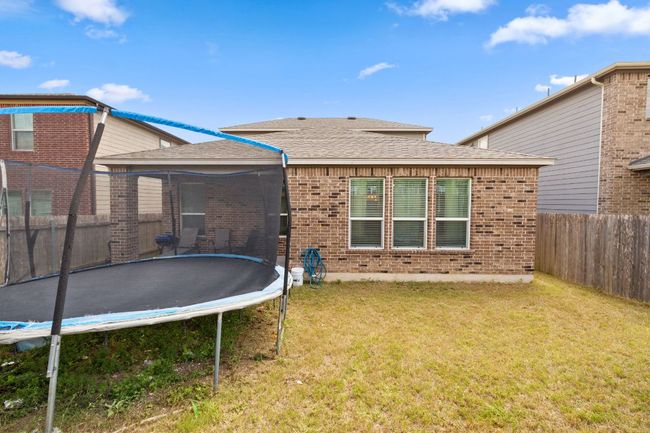Rear view of property with a trampoline, brick siding, a fenced backyard, and roof with shingles | Image 32