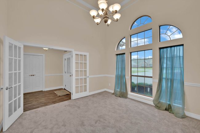 Carpeted empty room with french doors, a chandelier, and a high ceiling | Image 15