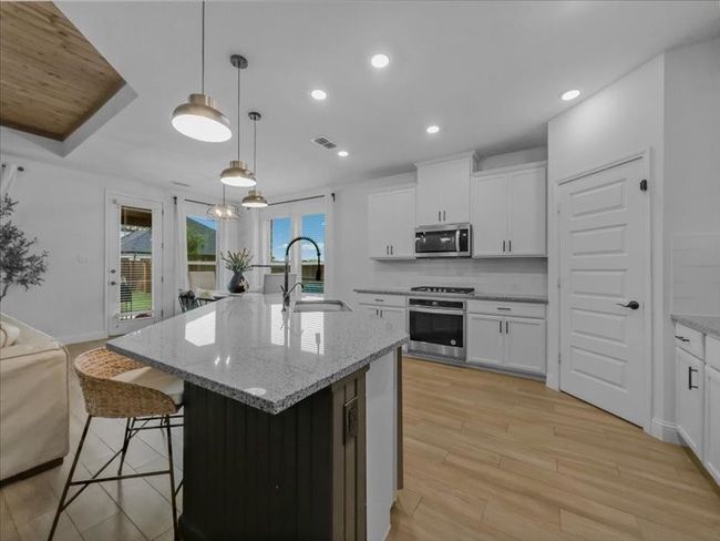 Kitchen with stainless steel appliances, a sink, light stone countertops, light wood-style flooring, and a center island with sink | Image 5