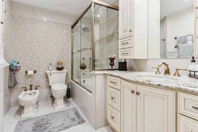 Full bathroom with bath / shower combo with glass door, vanity, toilet, a bidet, and tile patterned floors | Image 15