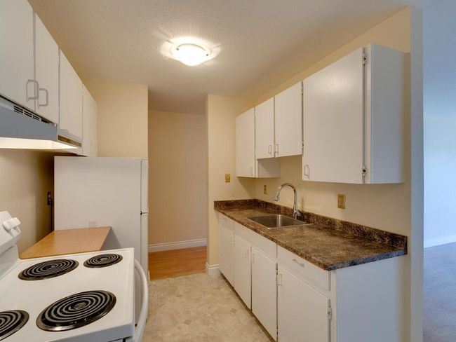 Kitchen with dark countertops, white cabinets, white appliances, a textured ceiling, and a sink | Image 12