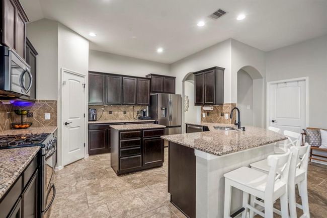 Imagine cooking in your kitchen with abundant counter and cabinet space. The island sits between the sink and pantry, while the eating bar by the sink makes a great spot for casual meals or conversation. Just beyond, the laundry room door sits next to the arched doorway leading back to your foyer. | Image 8