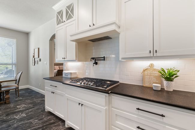 Kitchen with dark countertops, stainless steel gas cooktop, white cabinets, baseboards, and under cabinet range hood | Image 13