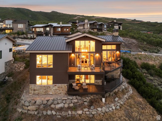 Back of property with stone siding, a balcony, a metal roof, a chimney, and a standing seam roof | Image 63