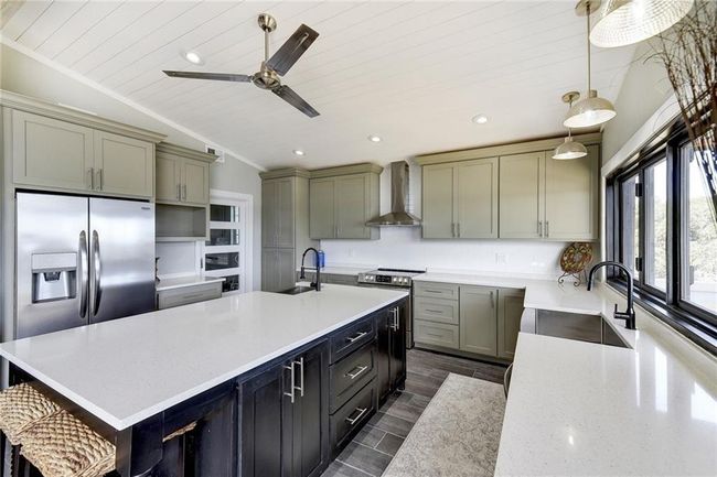 Kitchen with wall chimney exhaust hood, a sink, ceiling fan, an island with sink, and wood ceiling | Image 10