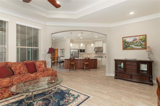 This inviting open-concept space features a cozy living area that flows seamlessly into a modern kitchen with stainless steel appliances, a central island, and elegant cabinetry. Large windows provide ample natural light, and the neutral color palette enhances the room's warmth and versatility. | Image 12