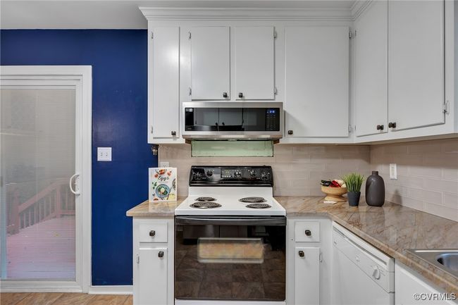 Updated kitchen featuring stainless steel microwave, electric range oven, dishwasher, and white cabinets, backsplash, custom built-in pantry and bar area, quartzite countertop, newer sliding patio doors with built-in blinds to porch and backyard | Image 13