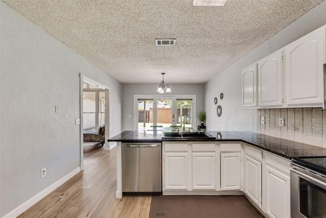 Kitchen featuring stainless steel appliances, a peninsula, white cabinets, light wood-type flooring, and a textured ceiling | Image 11