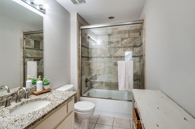 Full ensuite bath to the secondary bedroom upstairs: vanity, toilet, shower / bath combination with glass door, and tile floors | Image 19