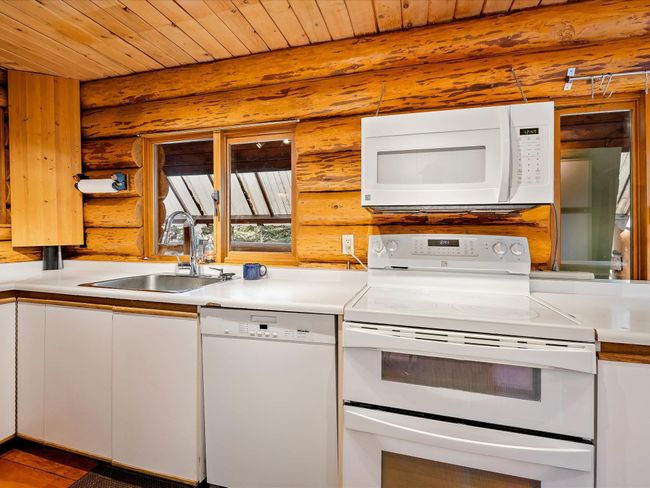 Kitchen with wooden ceiling, white appliances, white cabinets, and a sink | Image 9