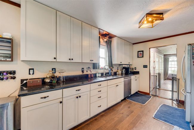 Kitchen with light wood-type flooring, a textured ceiling, white cabinets, a sink, and stainless steel appliances | Image 10