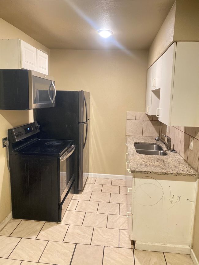Kitchen featuring black range with electric stovetop, a sink, white cabinets, light stone countertops, and stainless steel microwave | Image 5