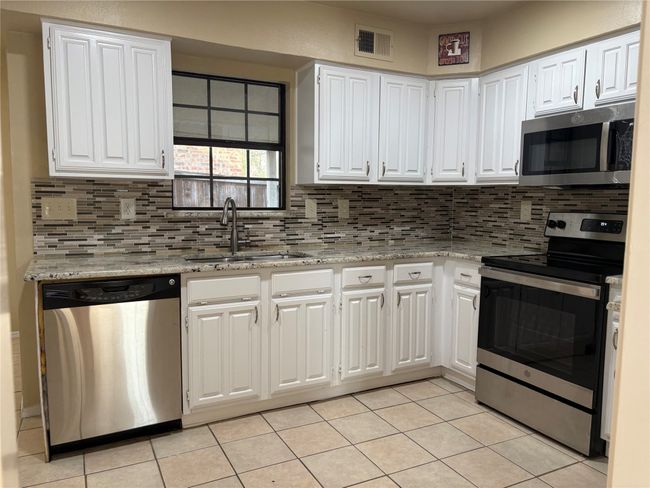 Kitchen featuring visible vents, stainless steel appliances, tasteful backsplash, white cabinetry, and a sink | Image 6