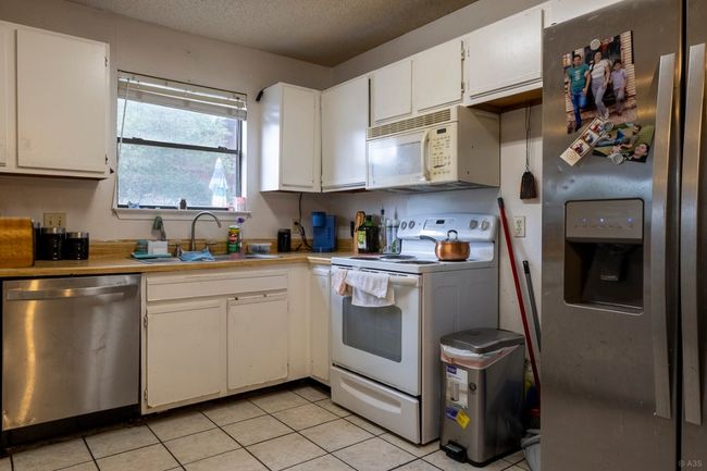 Kitchen with stainless steel appliances, a sink, light countertops, light tile patterned floors, and white cabinetry | Image 19