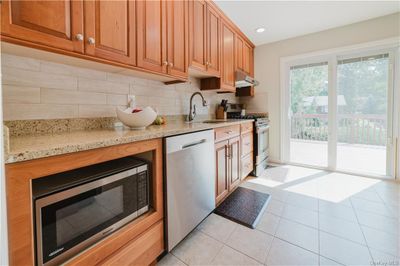 Kitchen with light stone countertops, light tile patterned floors, backsplash, appliances with stainless steel finishes, and sink | Image 3