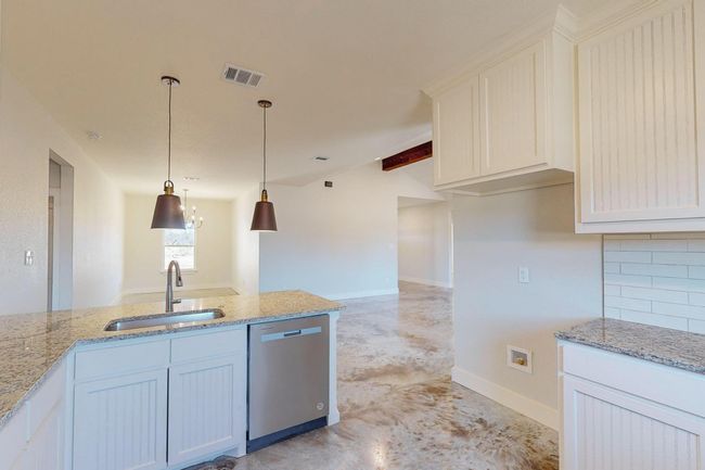Kitchen with finished concrete floors, stainless steel dishwasher, pendant lighting, light stone countertops, and tasteful backsplash | Image 16