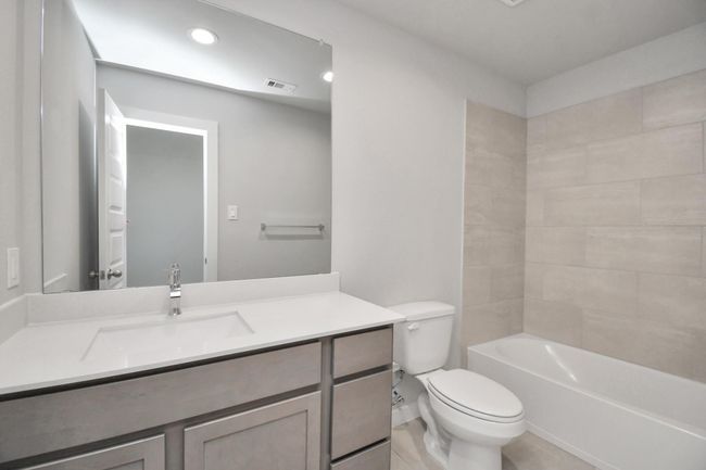 Secondary bath features tile flooring, bath/shower combo with tile surround, light stained wood cabinets, beautiful light countertop. | Image 31