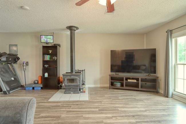 Living room with a wood stove, wood finished floors, a ceiling fan, and a textured ceiling | Image 21