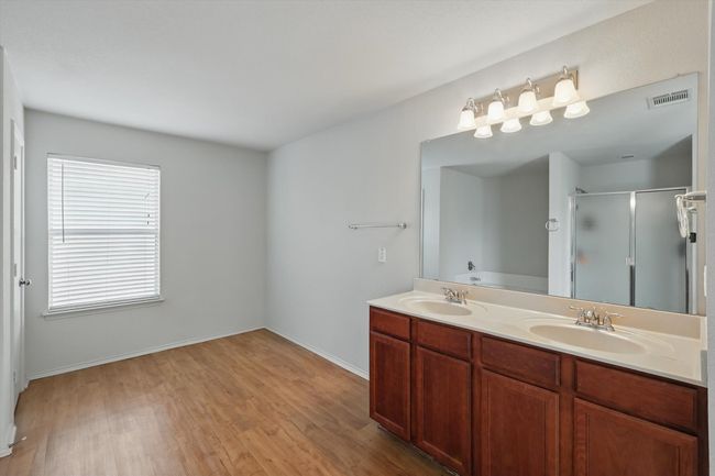 Bathroom featuring a stall shower, wood finished floors, double vanity, baseboards, and a garden tub | Image 11