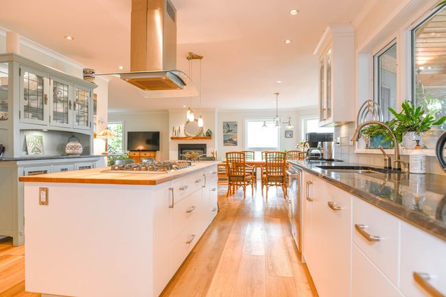 Kitchen featuring a sink, island range hood, stainless steel gas cooktop, wood counters, and a fireplace | Image 14