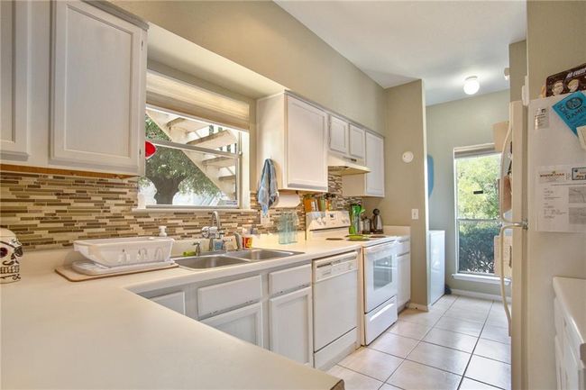 Kitchen featuring white appliances, a sink, light countertops, decorative backsplash, and under cabinet range hood | Image 8