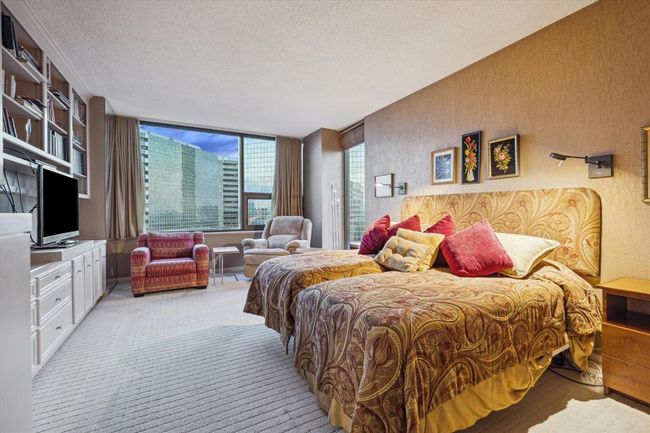 The spacious primary bedroom features built-in cabinetry and shelving, reading lights, space for a seating area, and large windows that bring in plenty of natural light. | Image 18