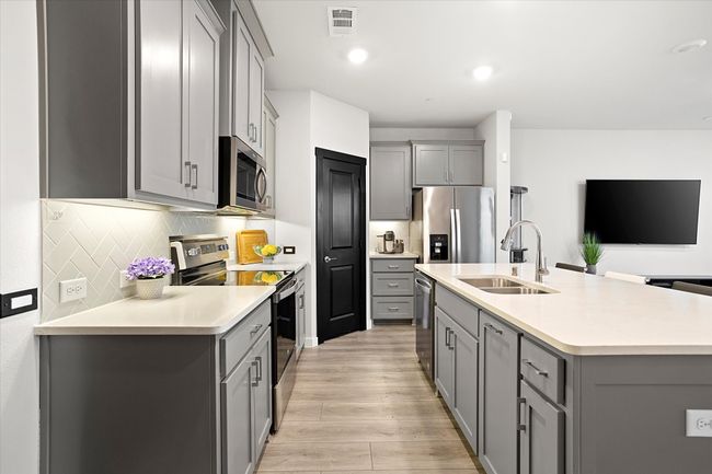 Kitchen featuring gray cabinets, stainless steel appliances, decorative backsplash, a kitchen island with sink, and recessed lighting | Image 10