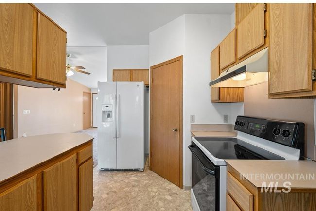 Kitchen with range with electric cooktop, white refrigerator with ice dispenser, under cabinet range hood, light countertops, and ceiling fan | Image 9