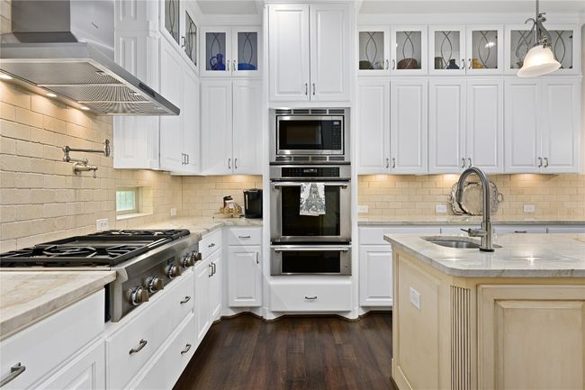 Kitchen featuring Thermador appliances with stainless steel finishes, wall chimney exhaust hood, a warming drawer, dark wood-style flooring, and a sink | Image 10