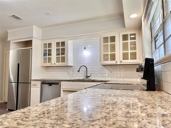 Kitchen with appliances with stainless steel finishes, light stone counters, backsplash, glass insert cabinets, and crown molding | Image 13