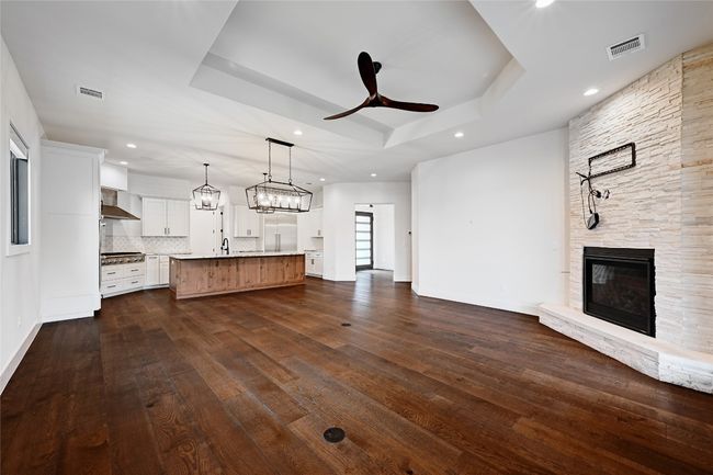 Unfurnished living room featuring a tray ceiling, visible vents, a stone fireplace, and ceiling fan | Image 7