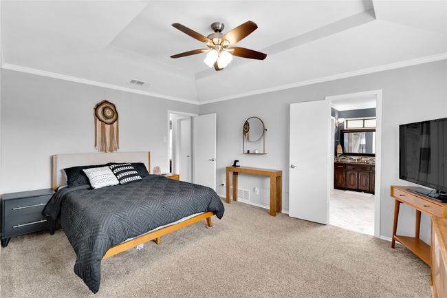 Carpeted bedroom featuring a tray ceiling, crown molding, ceiling fan, and connected bathroom | Image 23