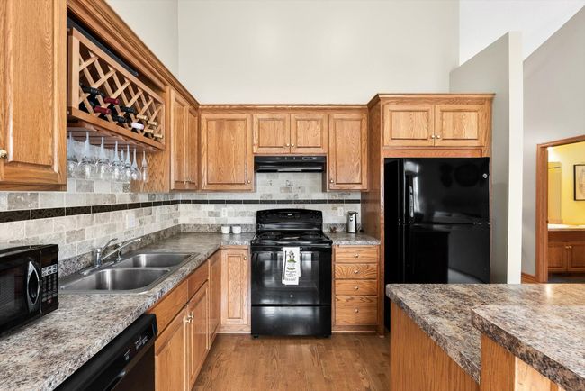 Spacious kitchen with vaulted ceilings, hardwood flooring, and an open-concept layout that flows into the dining and living areas. | Image 13