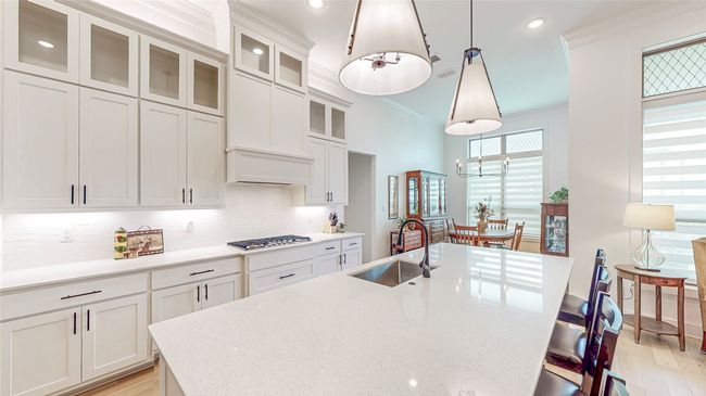Kitchen with a center island with sink, a kitchen breakfast bar, backsplash, white cabinets, and crown molding | Image 13