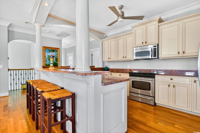Kitchen featuring stainless steel appliances, cream cabinets, decorative columns, crown molding, and a kitchen breakfast bar | Image 13