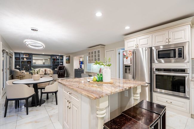 Kitchen featuring appliances with stainless steel finishes, a center island, light stone countertops, a chandelier, and decorative light fixtures | Image 12