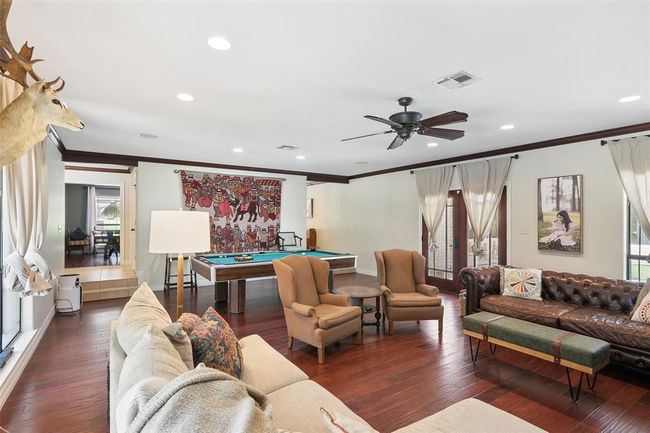 Spacious and inviting living area with hardwood floors, featuring a cozy seating arrangement, a pool table, and large windows for natural light. The room has a ceiling fan and decorative elements, creating a warm and entertaining space. | Image 12